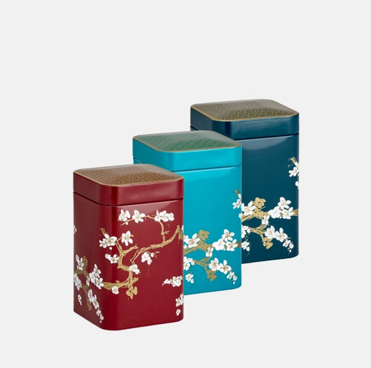 Three decorative tea canisters with floral designs on a white background